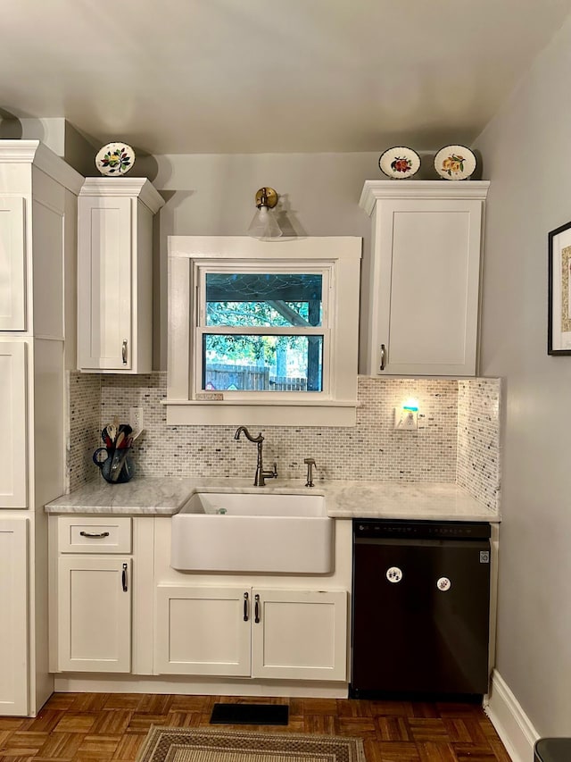 kitchen featuring black dishwasher, backsplash, white cabinetry, a sink, and light stone countertops