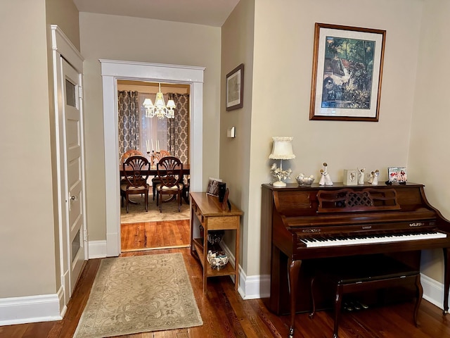 corridor featuring a chandelier, dark wood-style flooring, and baseboards