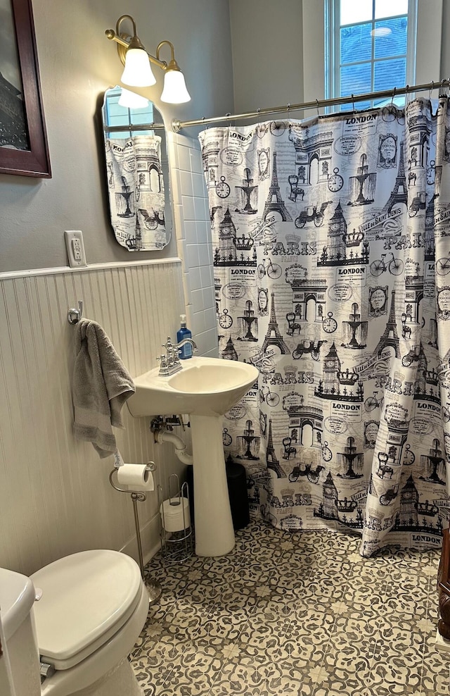 bathroom featuring toilet, a shower with curtain, and wainscoting