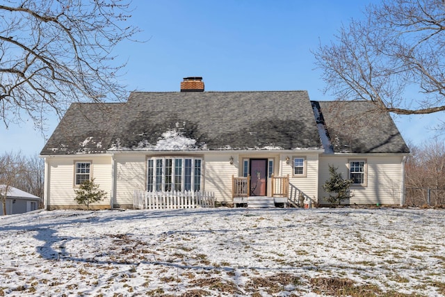 snow covered rear of property with a shingled roof and a chimney