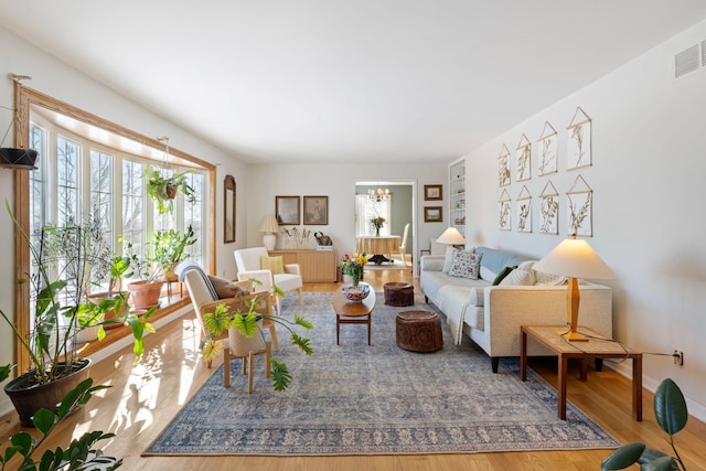 living area featuring baseboards, wood finished floors, visible vents, and an inviting chandelier