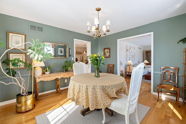 dining area featuring baseboards, light wood-style flooring, visible vents, and a notable chandelier