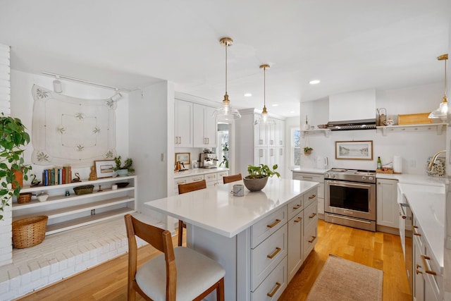 kitchen with light wood-style flooring, a kitchen island, light countertops, appliances with stainless steel finishes, and open shelves