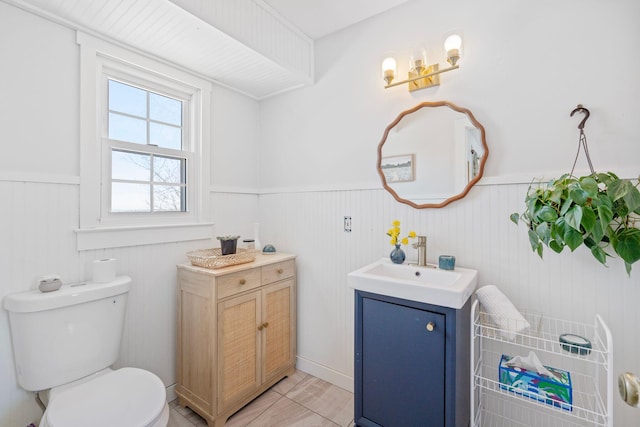 bathroom featuring a wainscoted wall, two vanities, a sink, and toilet