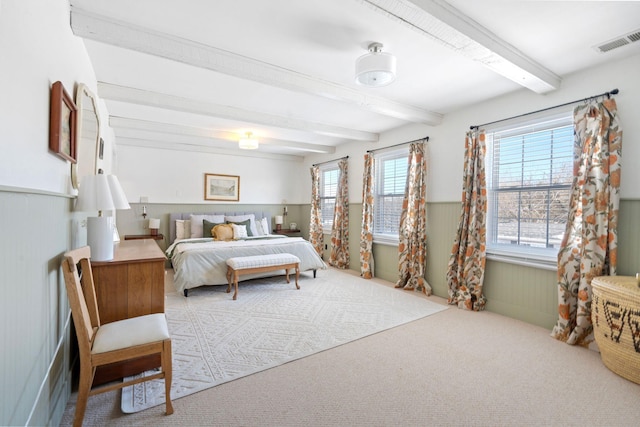 bedroom featuring carpet floors, visible vents, beamed ceiling, and wainscoting