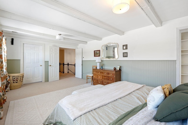 carpeted bedroom with wainscoting and beamed ceiling