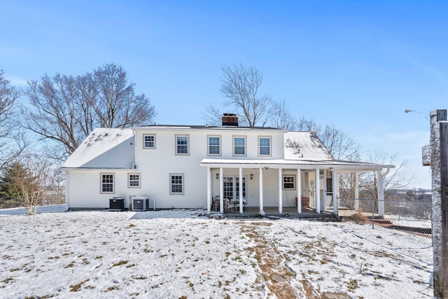 snow covered house featuring a porch, a chimney, central AC unit, and fence