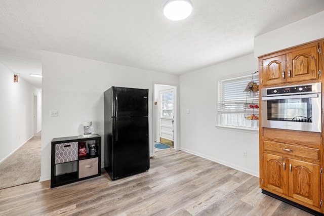 kitchen featuring oven, black fridge, a textured ceiling, and light hardwood / wood-style flooring