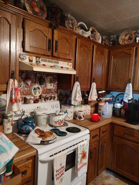 kitchen featuring brown cabinetry, electric range, light countertops, and under cabinet range hood