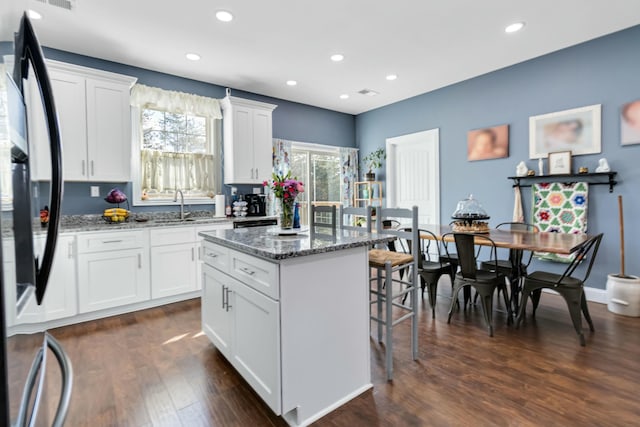 kitchen with white cabinets, a center island, sink, black fridge, and dark stone countertops