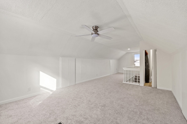 additional living space featuring ceiling fan, vaulted ceiling, a textured ceiling, and light colored carpet