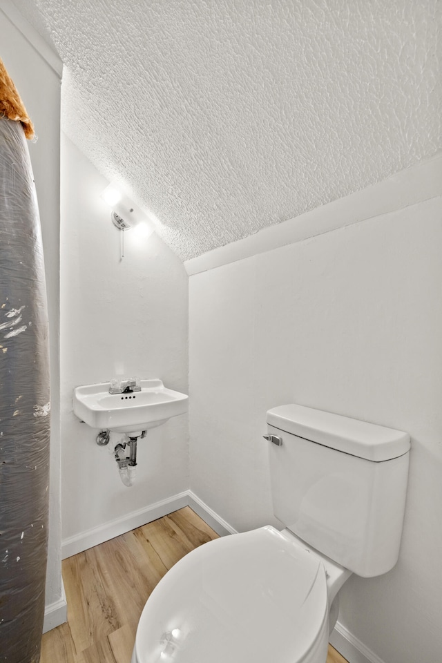 bathroom featuring hardwood / wood-style floors, vaulted ceiling, sink, a textured ceiling, and toilet