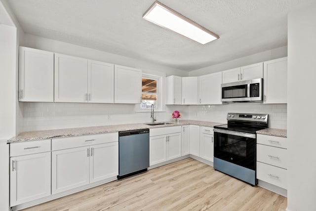 kitchen featuring appliances with stainless steel finishes, sink, white cabinetry, and light hardwood / wood-style floors