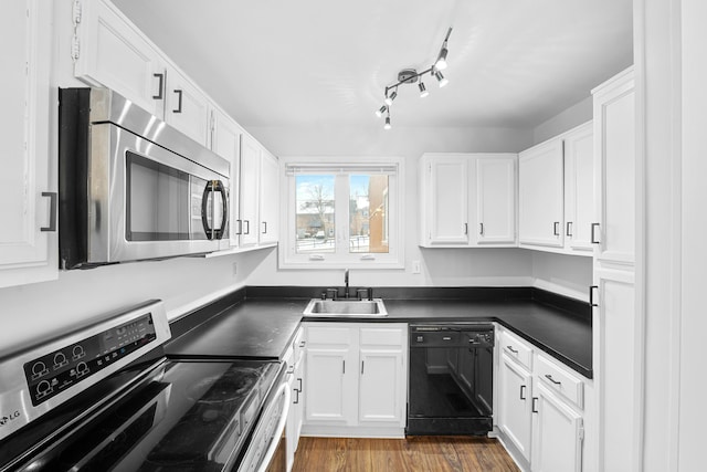 kitchen featuring dark countertops, appliances with stainless steel finishes, white cabinets, a sink, and light wood-type flooring