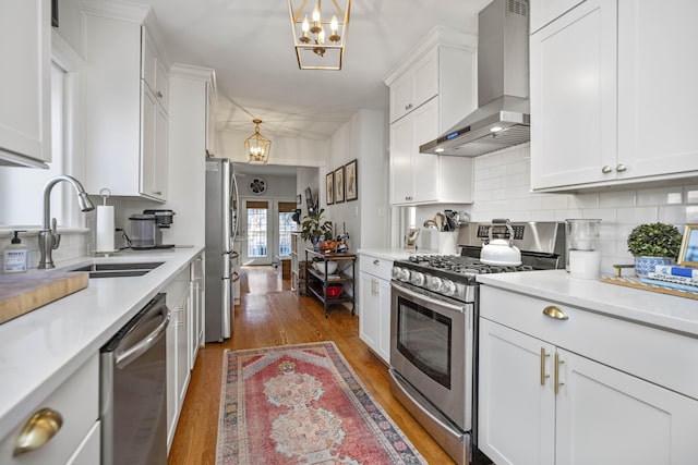 kitchen featuring wall chimney range hood, appliances with stainless steel finishes, sink, and pendant lighting