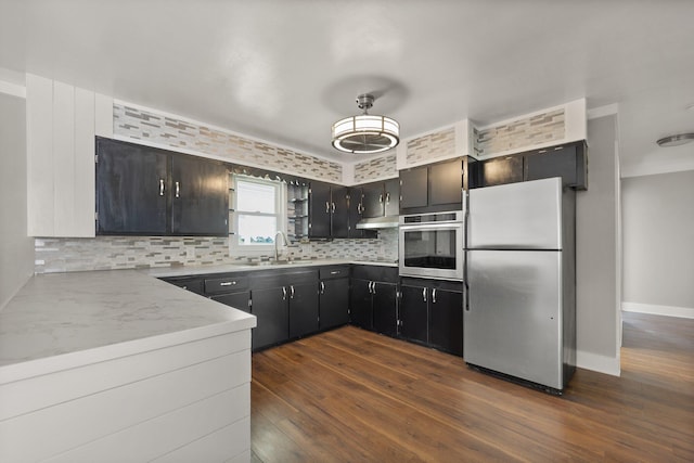 kitchen with dark wood-style flooring, a sink, light countertops, appliances with stainless steel finishes, and backsplash