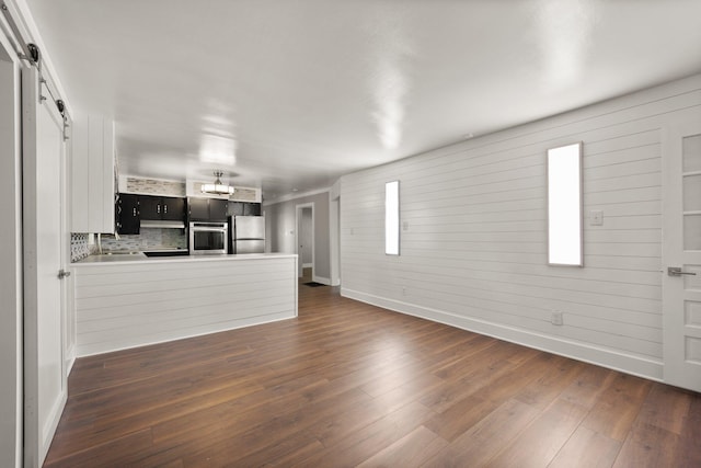 unfurnished living room with a sink, dark wood finished floors, baseboards, and a barn door