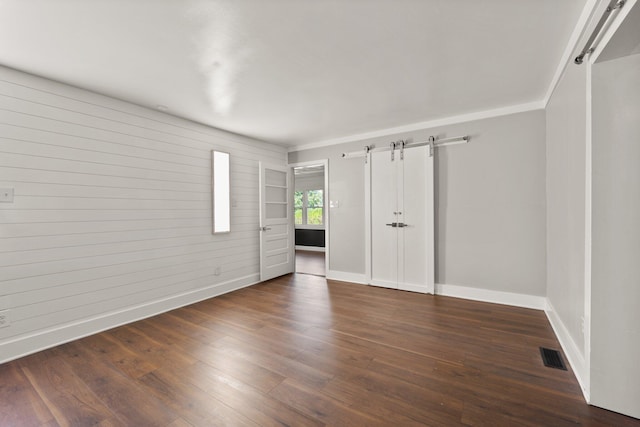 spare room with a barn door, wood finished floors, visible vents, and baseboards