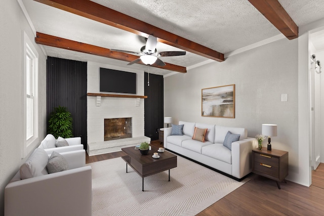 living room with a fireplace, beam ceiling, a textured ceiling, and wood finished floors