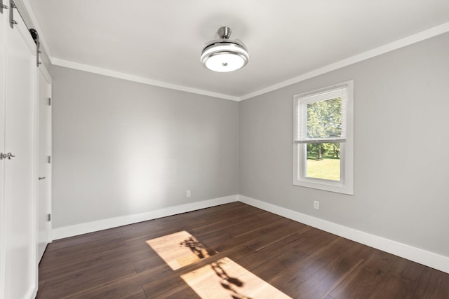 unfurnished room featuring baseboards, a barn door, dark wood-style flooring, and crown molding