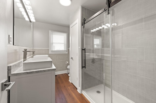 full bath featuring toilet, wood finished floors, tile walls, a sink, and a shower stall