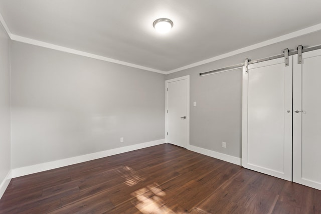 unfurnished bedroom with a barn door, baseboards, dark wood-type flooring, and ornamental molding