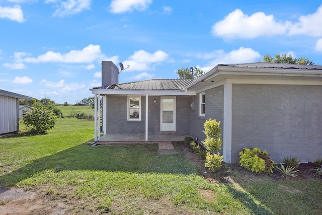 back of house featuring a chimney, metal roof, covered porch, a yard, and brick siding