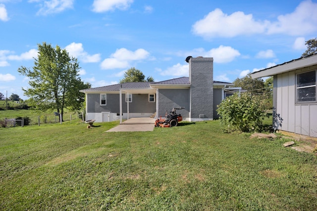 rear view of house with a patio, a chimney, metal roof, fence, and a yard