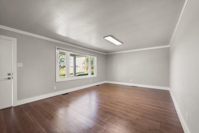 empty room featuring dark wood-style floors, visible vents, crown molding, and baseboards