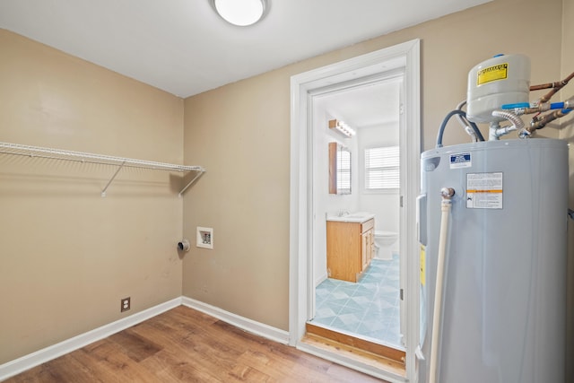 laundry room featuring water heater, laundry area, wood finished floors, and baseboards