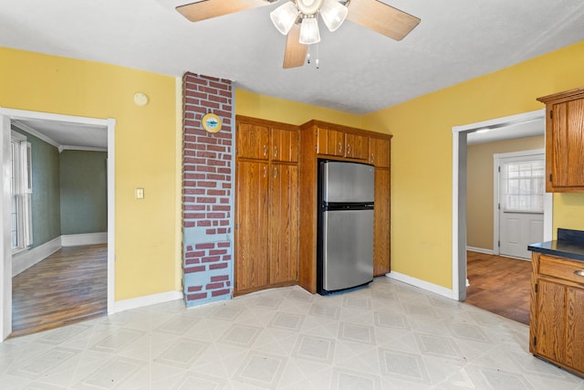 kitchen with brown cabinetry, dark countertops, freestanding refrigerator, and baseboards