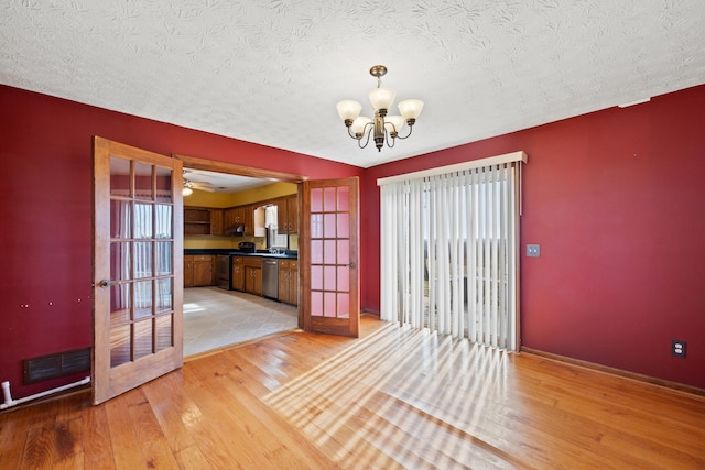 unfurnished dining area featuring a textured ceiling, light wood-style flooring, a notable chandelier, visible vents, and french doors