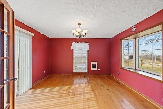 spare room with heating unit, a textured ceiling, a notable chandelier, and wood finished floors