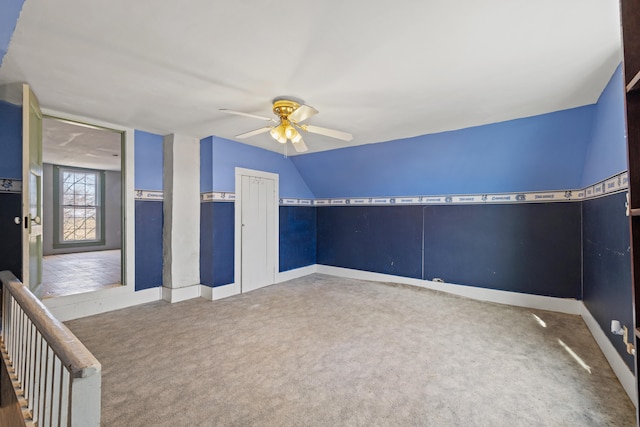 carpeted spare room featuring a ceiling fan, vaulted ceiling, and baseboards