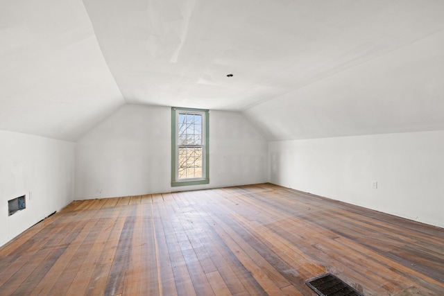 additional living space featuring lofted ceiling, visible vents, wood finished floors, and a glass covered fireplace