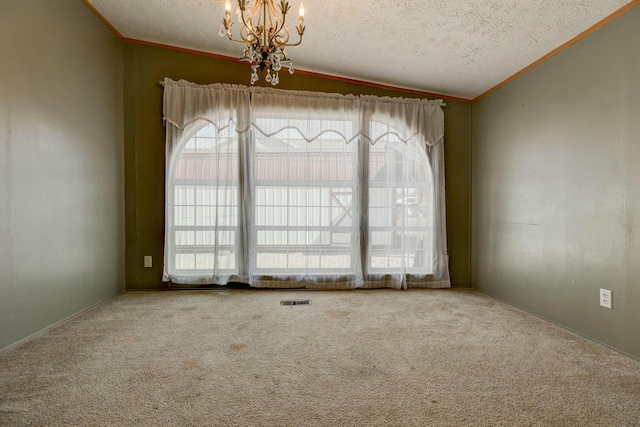 carpeted spare room featuring a chandelier, a textured ceiling, visible vents, and crown molding