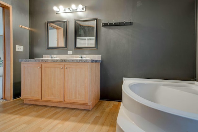 full bath with a tub, double vanity, a sink, and wood finished floors