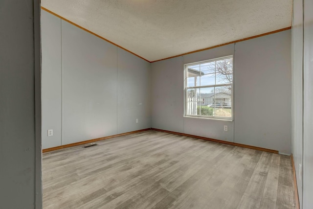 unfurnished room featuring lofted ceiling, visible vents, light wood-style flooring, ornamental molding, and a textured ceiling