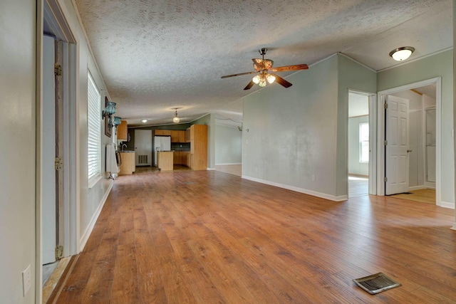 unfurnished living room with baseboards, visible vents, light wood-style flooring, ceiling fan, and a textured ceiling