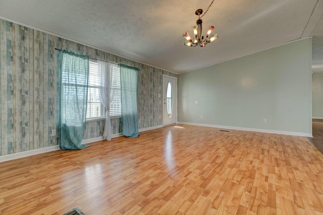 empty room with light wood-type flooring, an inviting chandelier, baseboards, and a textured ceiling