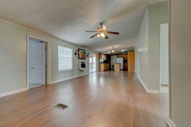 unfurnished living room featuring heating unit, visible vents, vaulted ceiling, ceiling fan, and light wood-type flooring