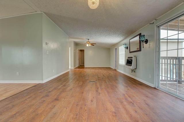 unfurnished living room with a ceiling fan, a healthy amount of sunlight, heating unit, and wood finished floors