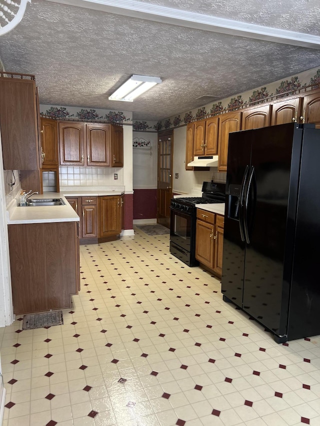 kitchen featuring under cabinet range hood, light countertops, a textured ceiling, black appliances, and a sink