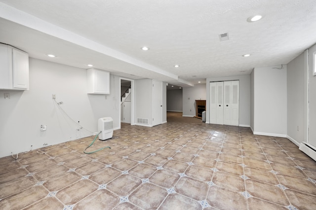 finished below grade area featuring baseboards, visible vents, stairs, a textured ceiling, and recessed lighting