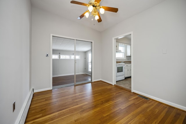 unfurnished bedroom with a baseboard heating unit, dark wood-style flooring, visible vents, baseboards, and a closet