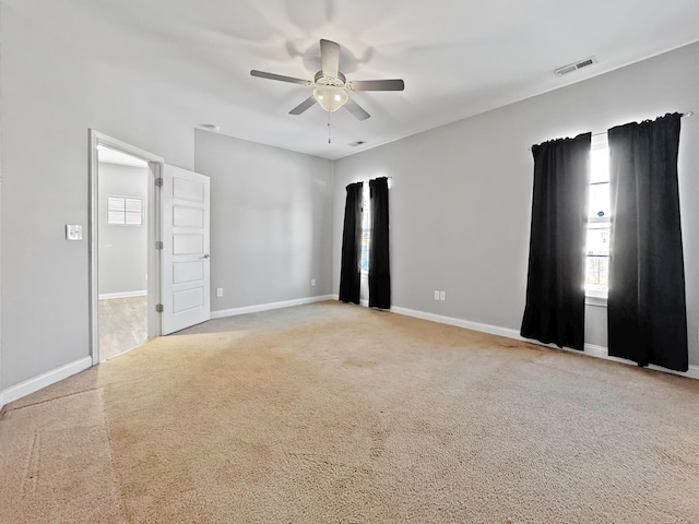 empty room featuring baseboards, visible vents, ceiling fan, and light colored carpet