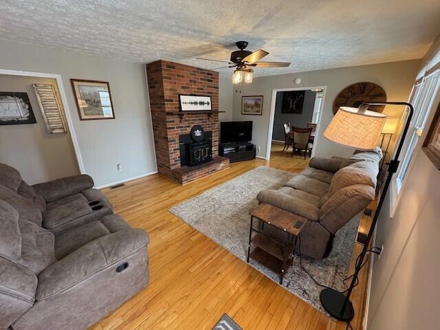 living room with a wood stove, wood-type flooring, a textured ceiling, and ceiling fan