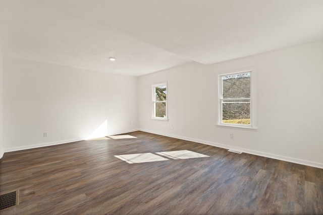 spare room featuring dark wood-style flooring, visible vents, and baseboards