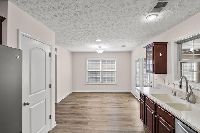 kitchen featuring visible vents, dishwasher, wood finished floors, light countertops, and a sink