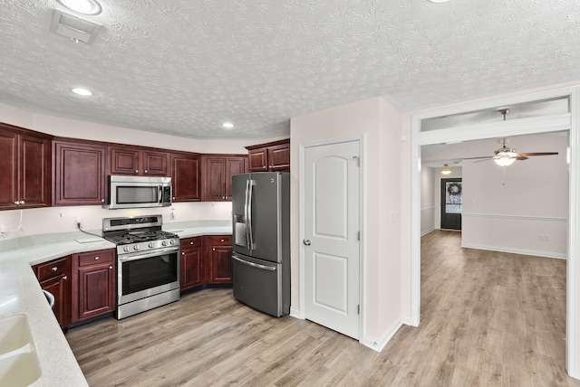 kitchen featuring reddish brown cabinets, light wood finished floors, appliances with stainless steel finishes, and light countertops